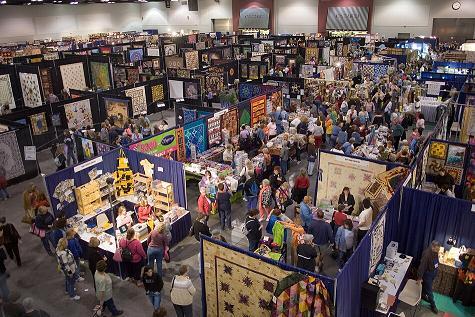 overhead view of large quilt conference showing vendors booths and quilts hanging in a crowded exhibit