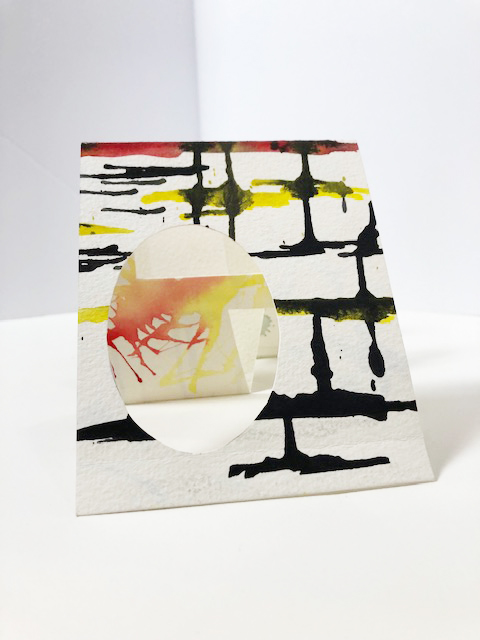 accordion folded watercolor paper with geometric shapes cut out, black yellow and red abstract marks painted